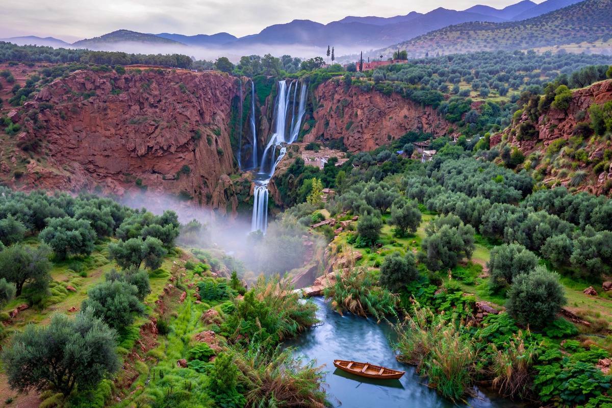 Ouzoud waterfalls cascading in three tiers down rust-red cliffs into a green gorge of olive trees