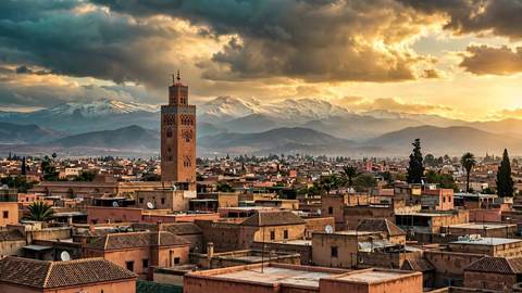 Le minaret de la Koutoubia dominant les toits de la médina de Marrakech à l'heure dorée, avec les sommets enneigés de l'Atlas en arrière-plan