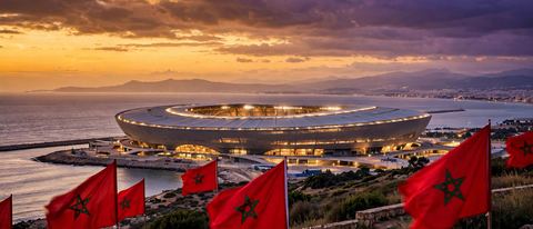 Grand Stade de Tanger illuminé au crépuscule avec un toit complet et des drapeaux marocains, le détroit de Gibraltar et la côte espagnole à l'horizon